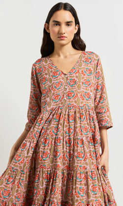 Plümo- Woman wearing the Nila Flower Dress, a block-printed floral midi in pink, red, and green on a beige background.