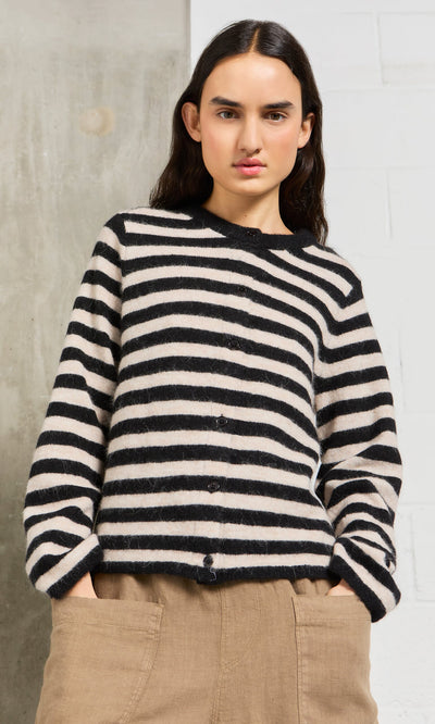 Plümo- A person wears the Nola Stripe Cardigan and tan pants, standing with hands in pockets against a light background.