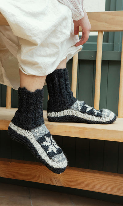 Plümo  Person wearing Nordic Star Slipper Socks sits on a wooden bench.