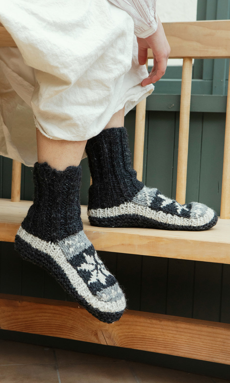 Plümo  Person wearing Nordic Star Slipper Socks sits on a wooden bench.
