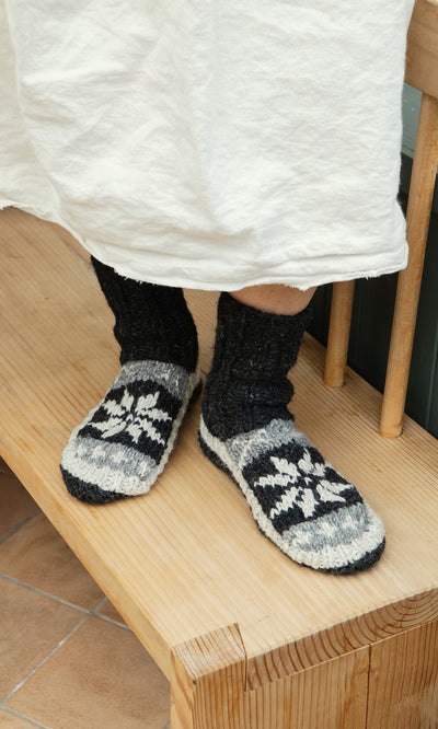Plümo  Person in Nordic Star Slipper Socks stands on wooden bench, white skirt partially visible.