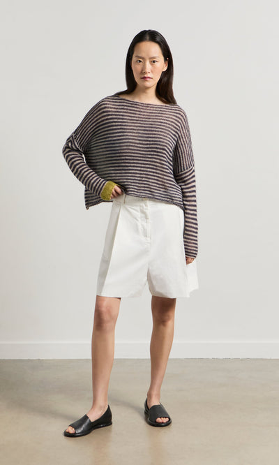 Plümo- Woman wearing a Paloma Stripe Sweater, white knee-length shorts, and black open-toe sandals indoors.