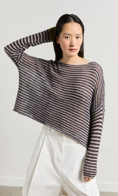 Plümo- Woman in the Paloma Stripe Sweater and white shorts, posing with one hand behind her head.