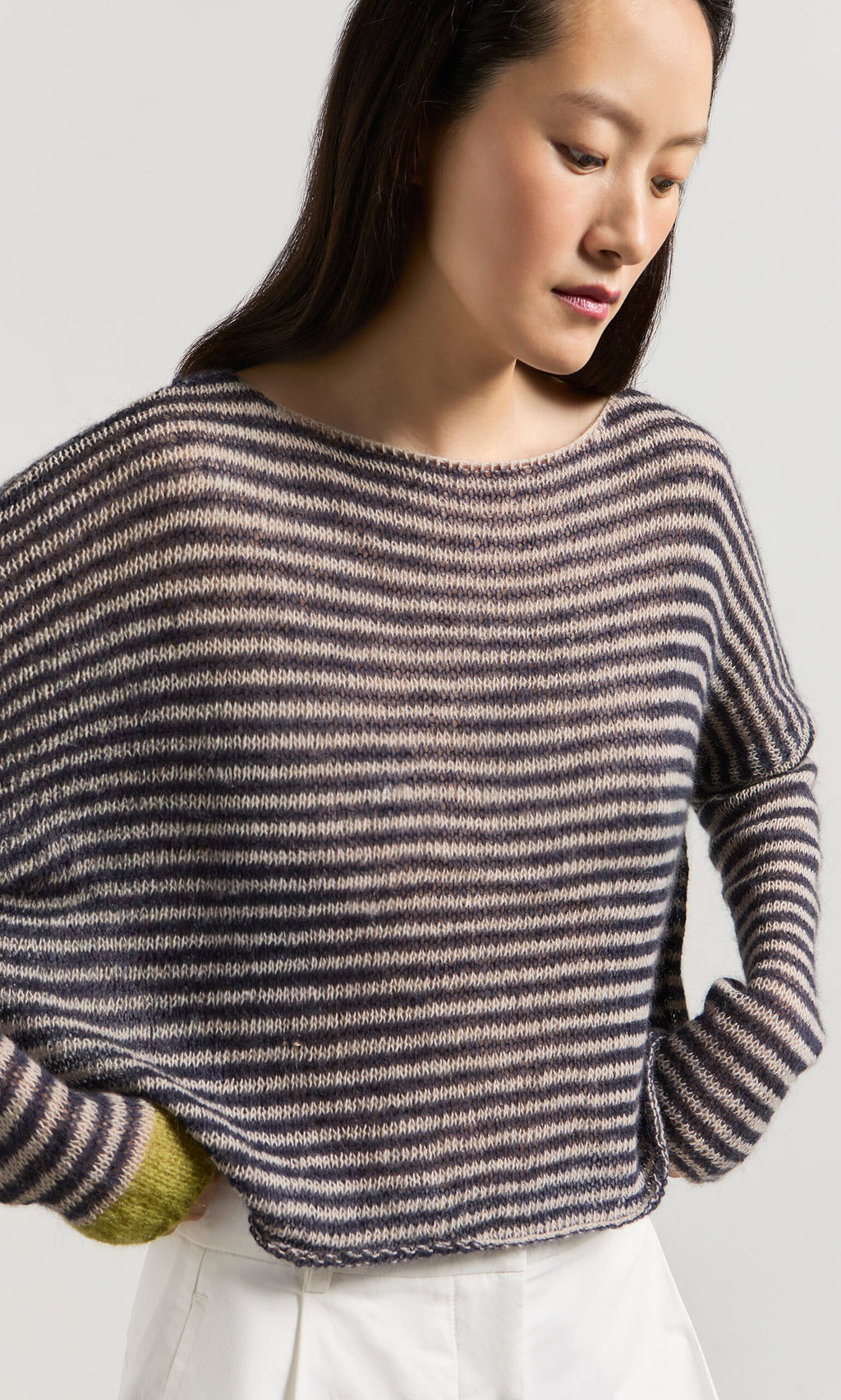 Plümo- Woman in the Paloma Stripe Sweater—lightweight, long-sleeve knit with horizontal stripes—paired with white pants.