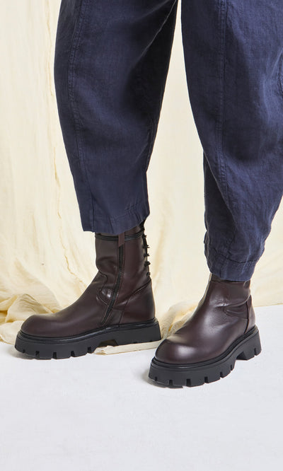 Plümo- Person wearing Paola Boots—artisan crafted, dark brown Italian leather with thick soles—paired with navy blue pants.