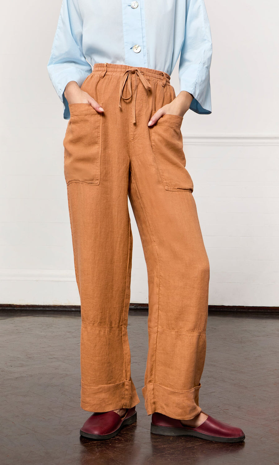Plümo- Person wearing light blue shirt, maroon slip-on shoes, and Pecan Pocket Pants with drawstring waistband indoors.