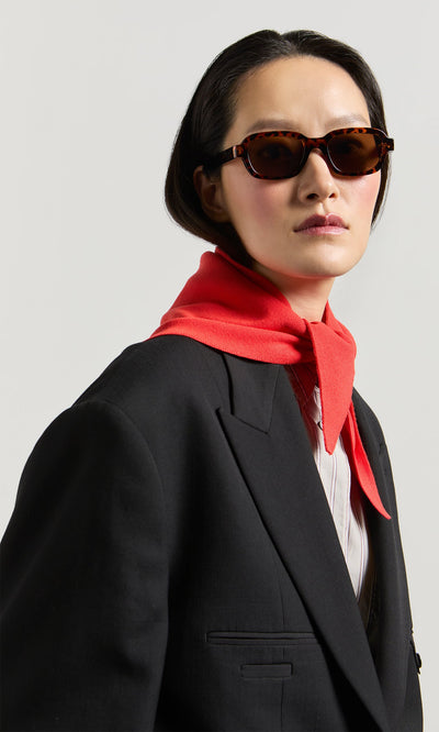 Plümo- Woman wearing Portia Sunglasses, a black blazer, red scarf, and white shirt, looking confidently at the camera.