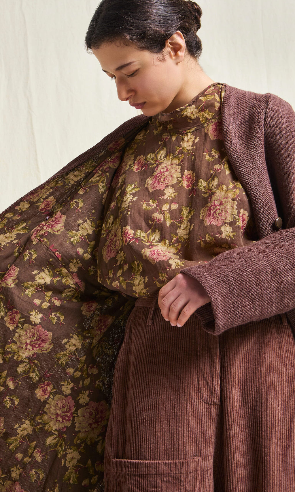 Plümo- Woman in a brown coat reveals its floral lining, layering over the Sylvie Shirt against a neutral background.