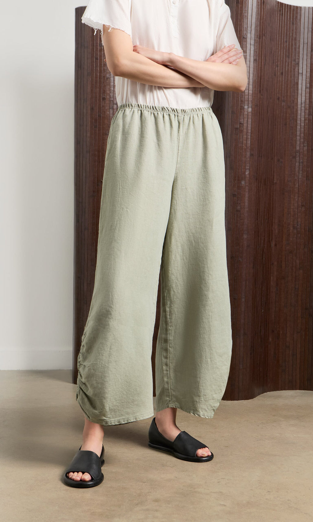 Plümo- Person in Royles Pants with elasticated waist, white shirt, and black slides stands indoors with arms crossed.