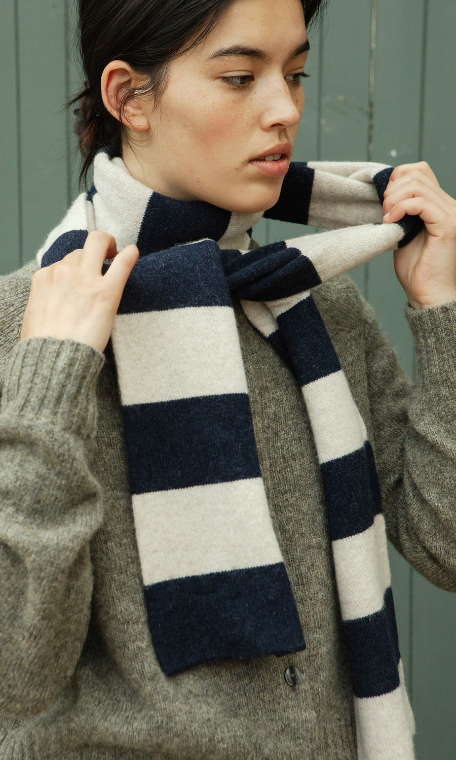 Plümo  Person in a gray sweater tying the Rugby Stripe Scarf, featuring navy and white stripes, around their neck.