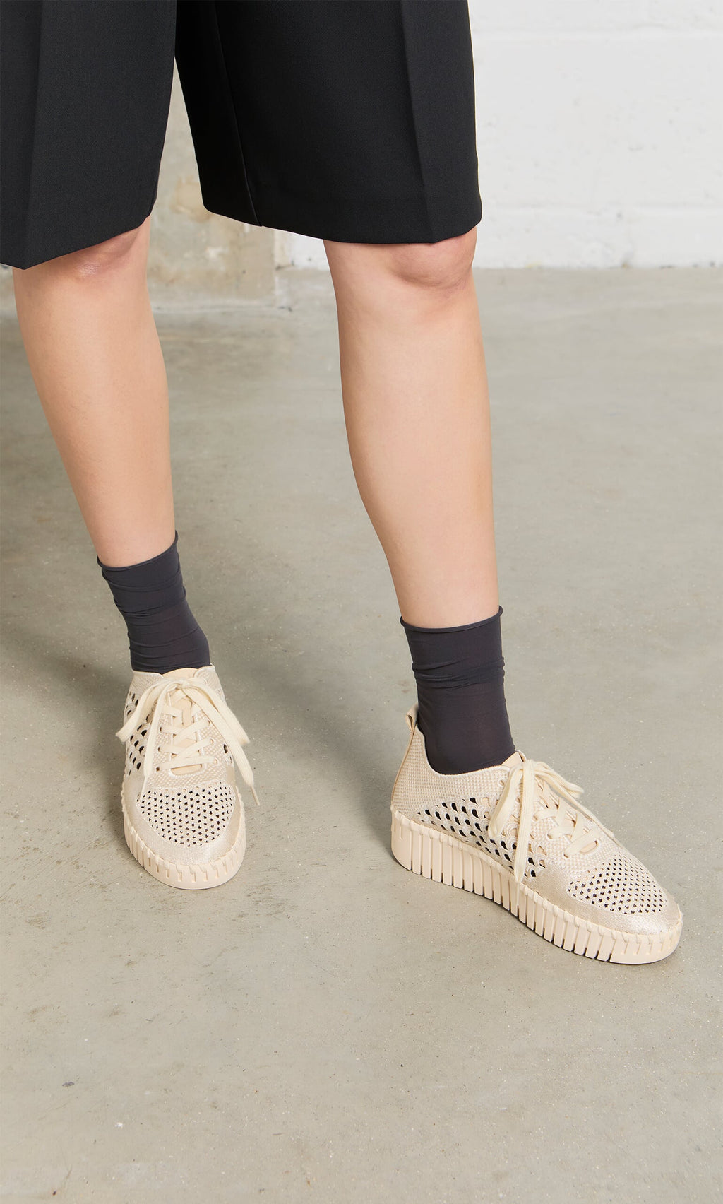 Plümo- Person wears black shorts, dark socks, and Runa Trainers with a breathable embroidered upper on concrete.