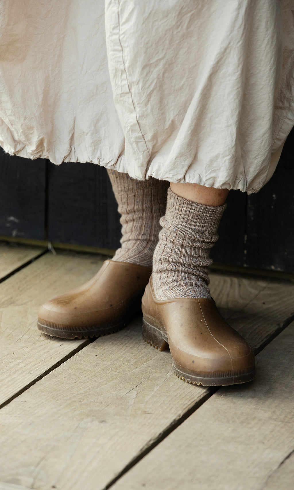 Plümo  Person wears Oatmeal Socks and brown clogs on wood floor, cream skirt hem just above their shoes.