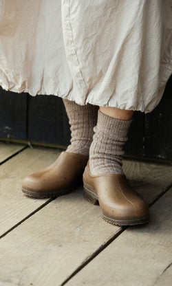 Plümo  Person wears Oatmeal Socks and brown clogs on wood floor, cream skirt hem just above their shoes.
