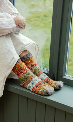 Plümo  Person sitting by a window in a cream skirt and Sofa Socks, hands on knees, savoring the moment.