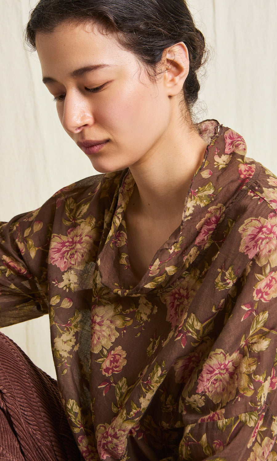 Plümo- Woman wears the Sylvie Shirt, a lightweight cotton floral cowl neck top, against a light neutral background.