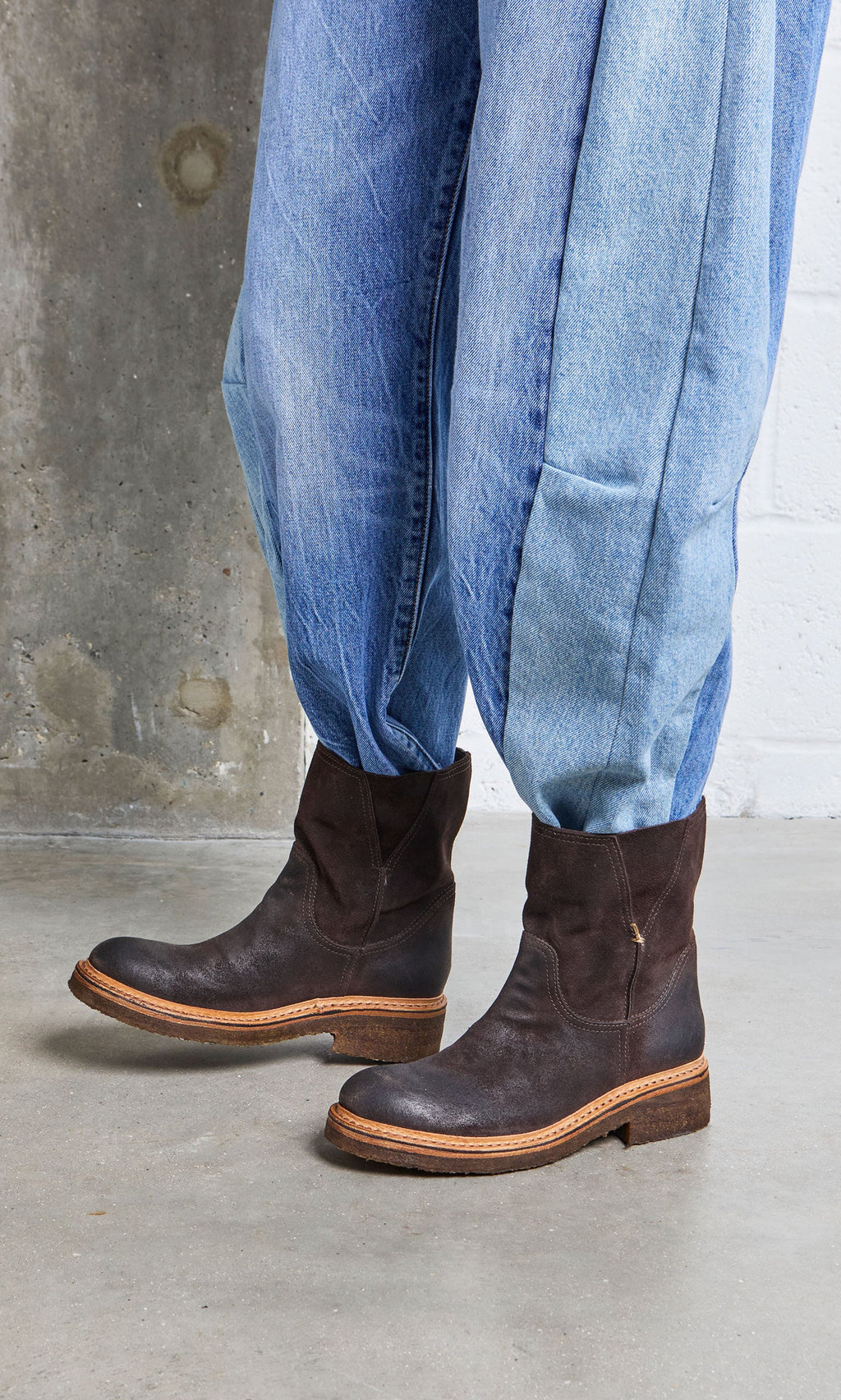 Plümo- Person wearing loose, light blue jeans and Tait Boots, handmade in Italy, standing on a concrete floor.