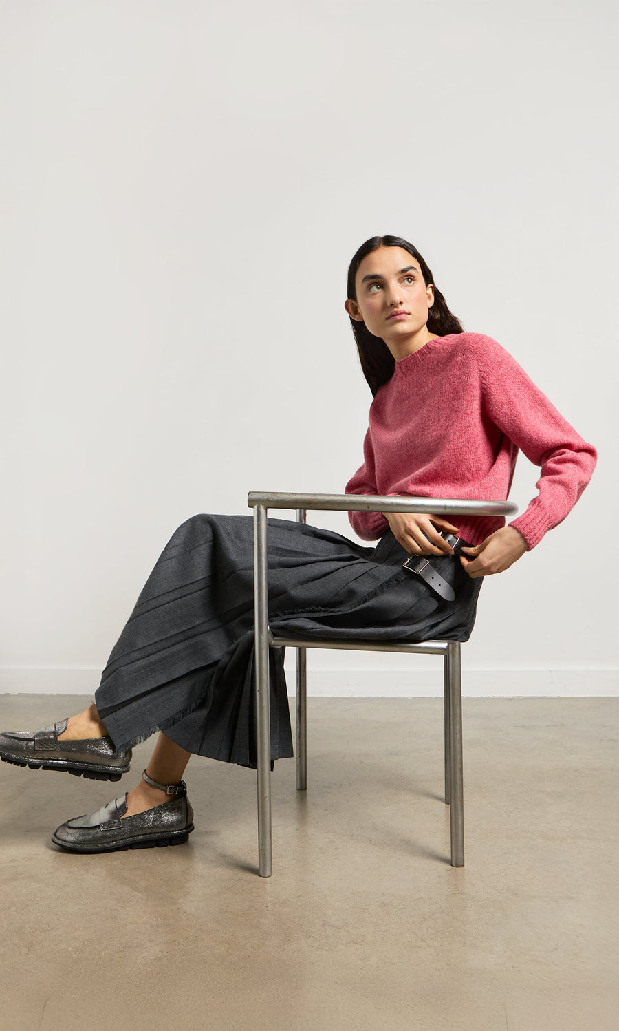 Plümo- Woman in a metal chair wearing a pink sweater and the Boyd Kilt, made in Ireland, looking to the side.