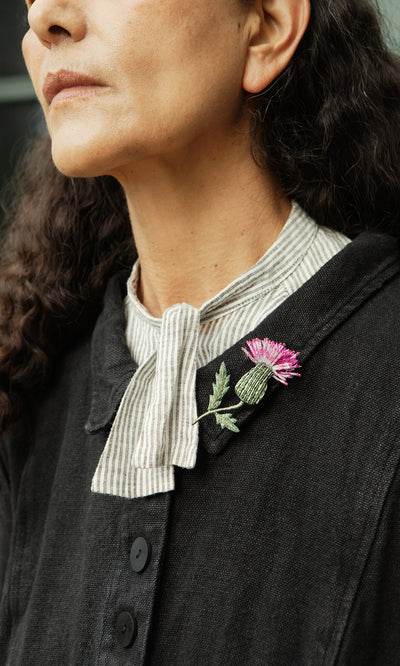 Plümo  Woman in a dark coat with a striped shirt, wearing a Thistle Brooch on her collar.
