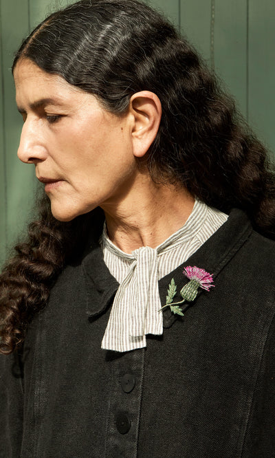 Plümo  Woman with long curly hair, in a scarf and black coat, wears the Thistle Brooch on her collar.