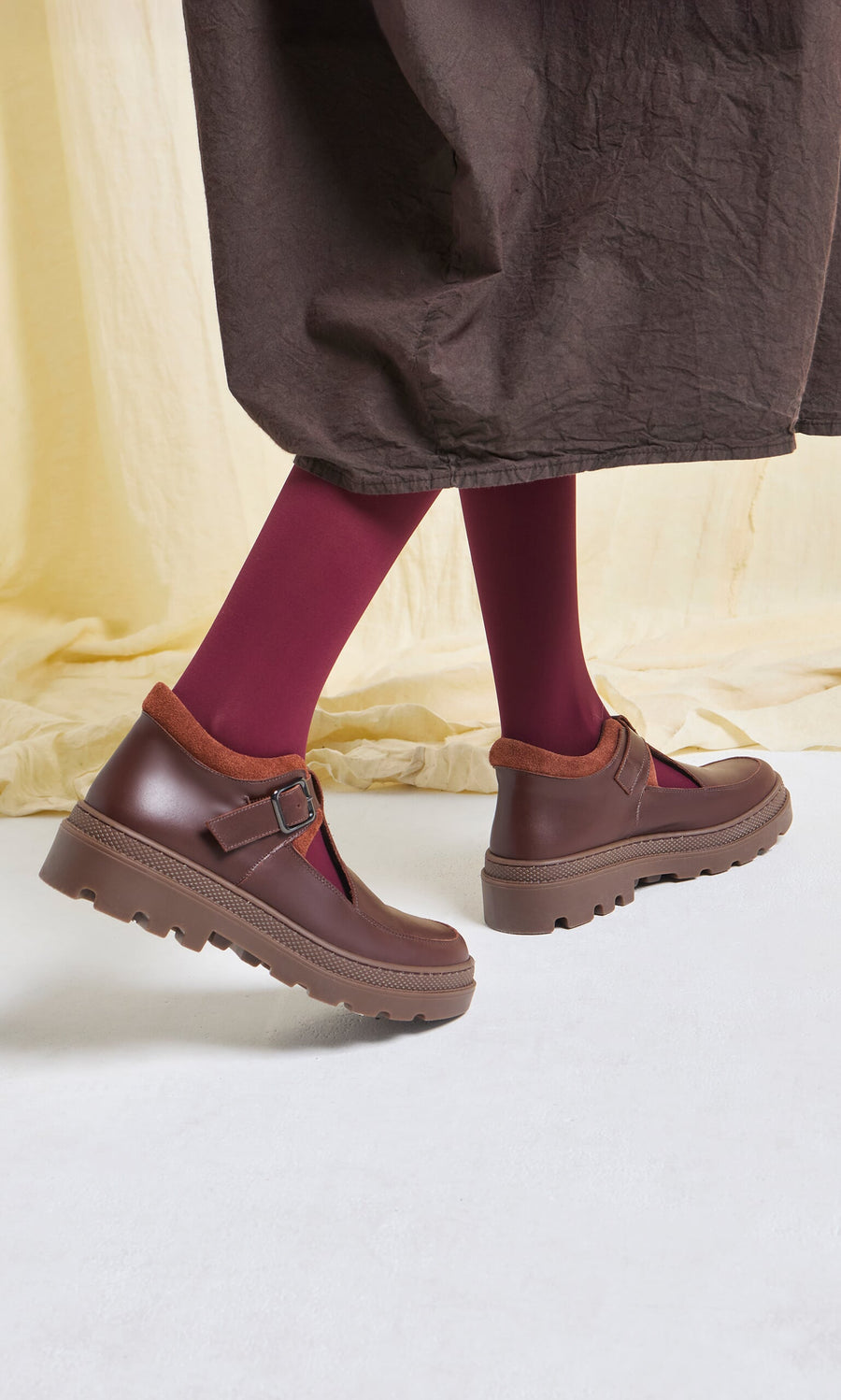 Plümo- Woman wearing burgundy tights and brown Toba Shoes with grooved rubber soles, standing on a white floor.