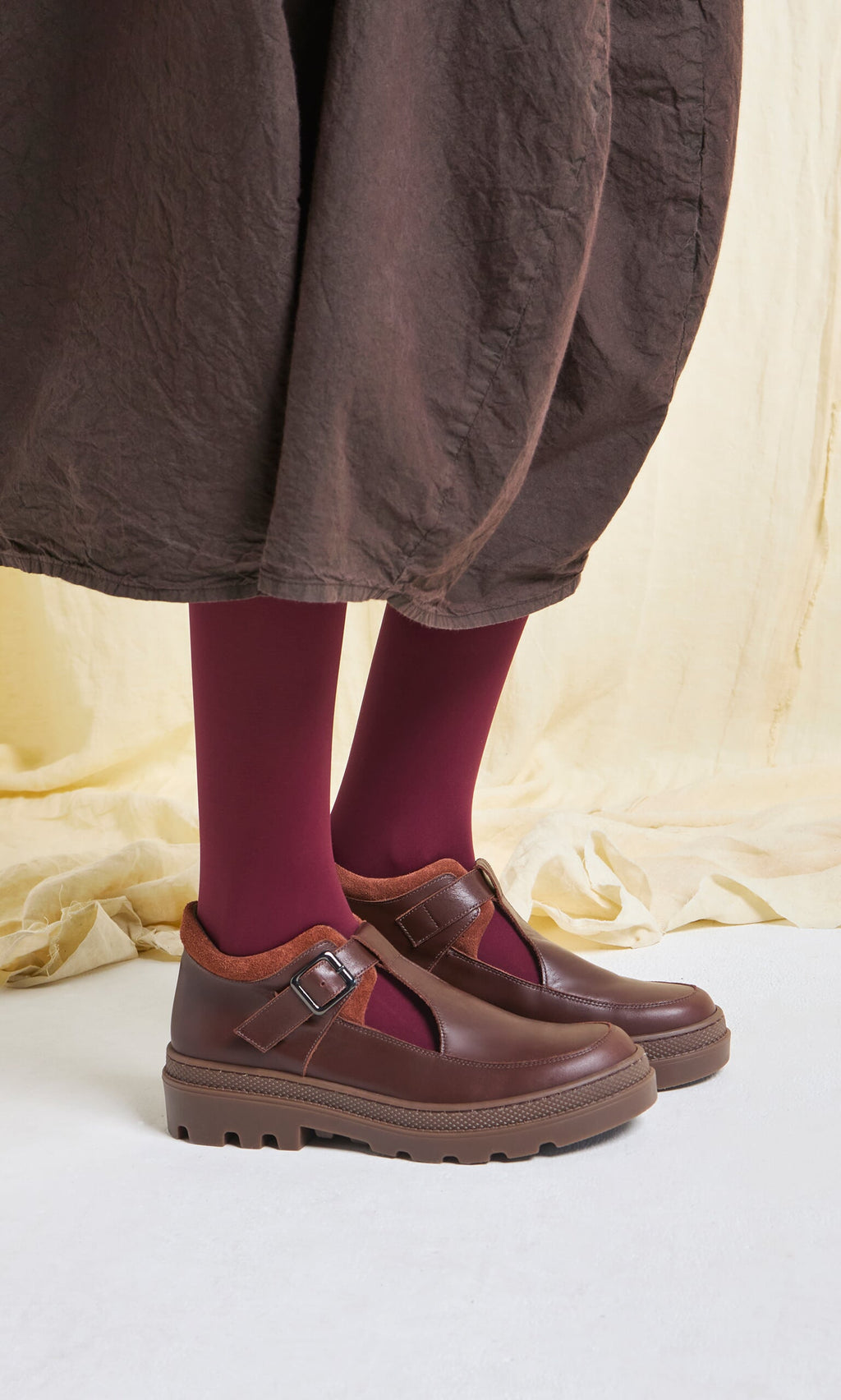 Plümo- Person wearing burgundy tights and Toba Shoes with a grooved rubber sole, on a light surface and beige backdrop.