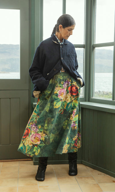Plümo  Woman in Dunbar Tweed Jacket stands indoors by windows, looking down with hands in pockets.
