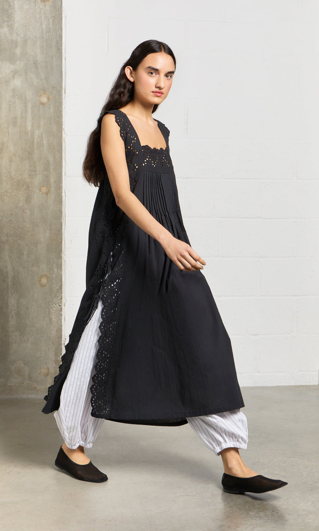 Plümo- Woman wears a Vintage Lace Dress with white striped pants and black flats, walking indoors.