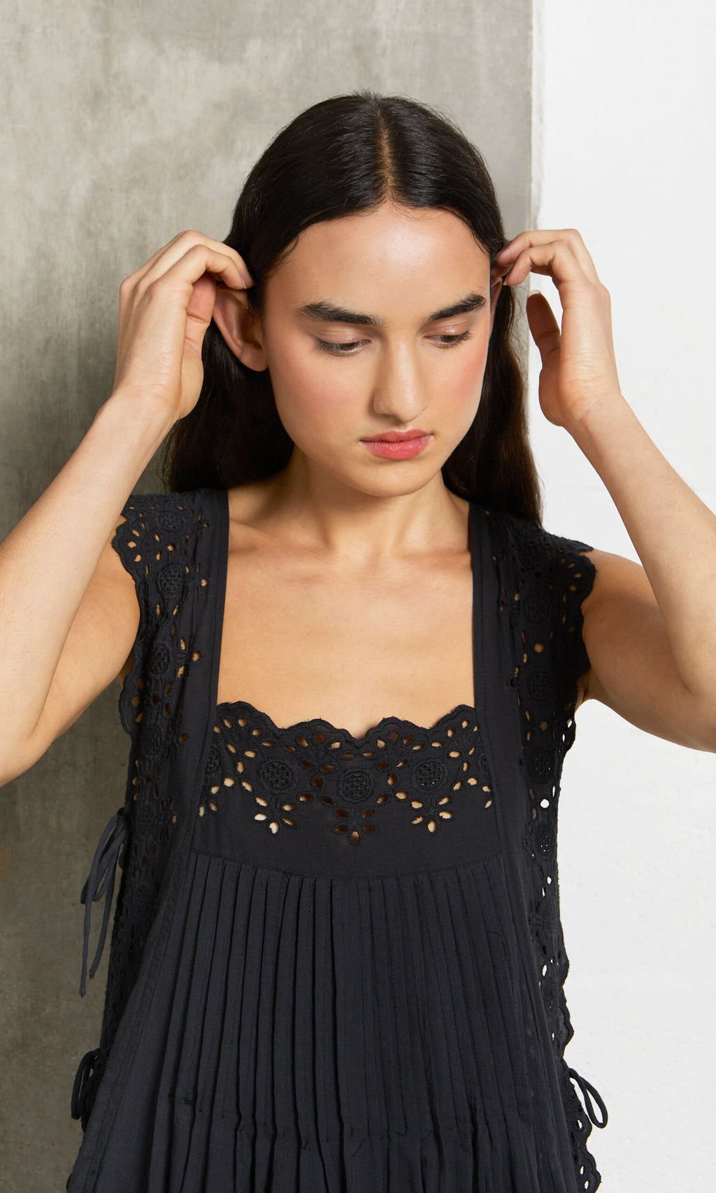 Plümo- Woman with long dark hair in a sleeveless Vintage Lace Dress, looking down and touching her hair with both hands.