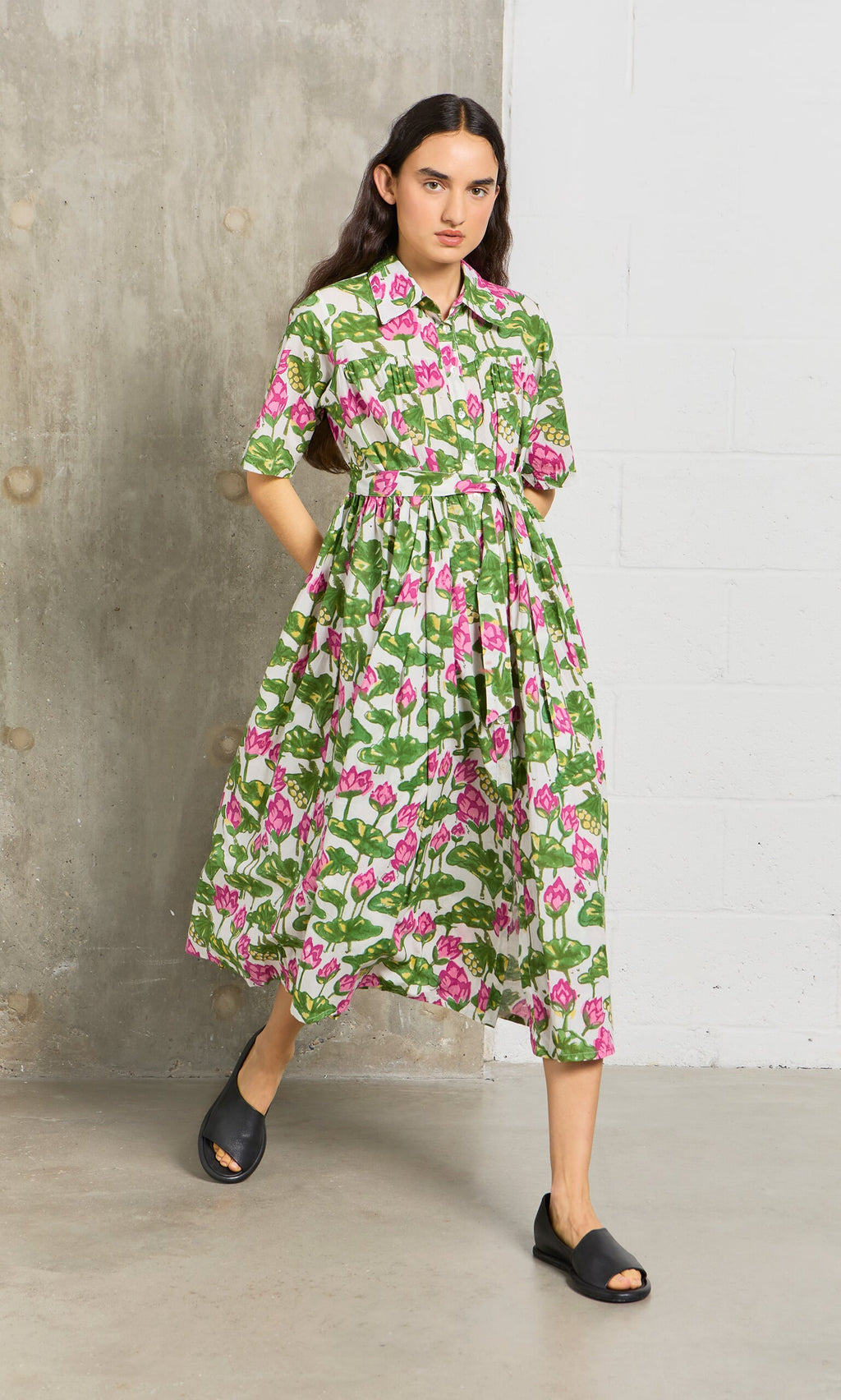 Plümo- Person in a green and pink Waterlily Dress with black sandals, walking indoors.