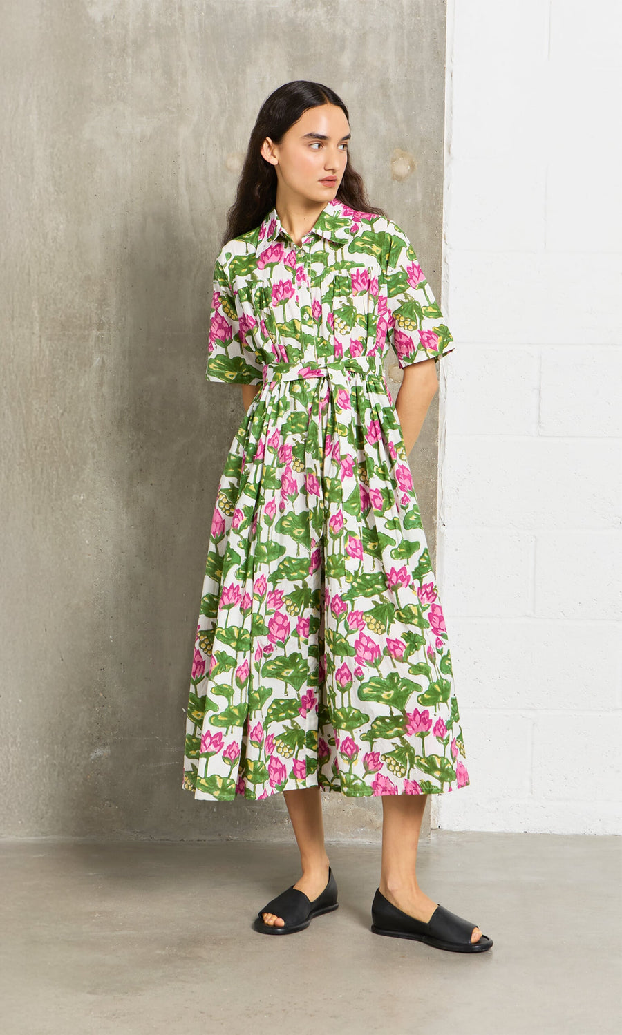 Plümo- Woman in the Waterlily Dress—pink and green cotton-voile with tiered gathers—stands indoors in black sandals.