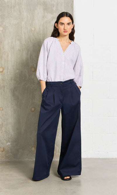 Plümo- Woman wears Wide Navy Chinos with a wide-leg silhouette, hands in pockets, paired with a striped blouse indoors.