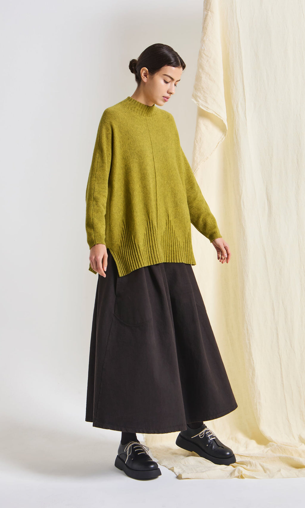 Plümo- Woman wears the Wild Millet Jumper, a loose marled sweater, styled with a wide black skirt against a neutral background.