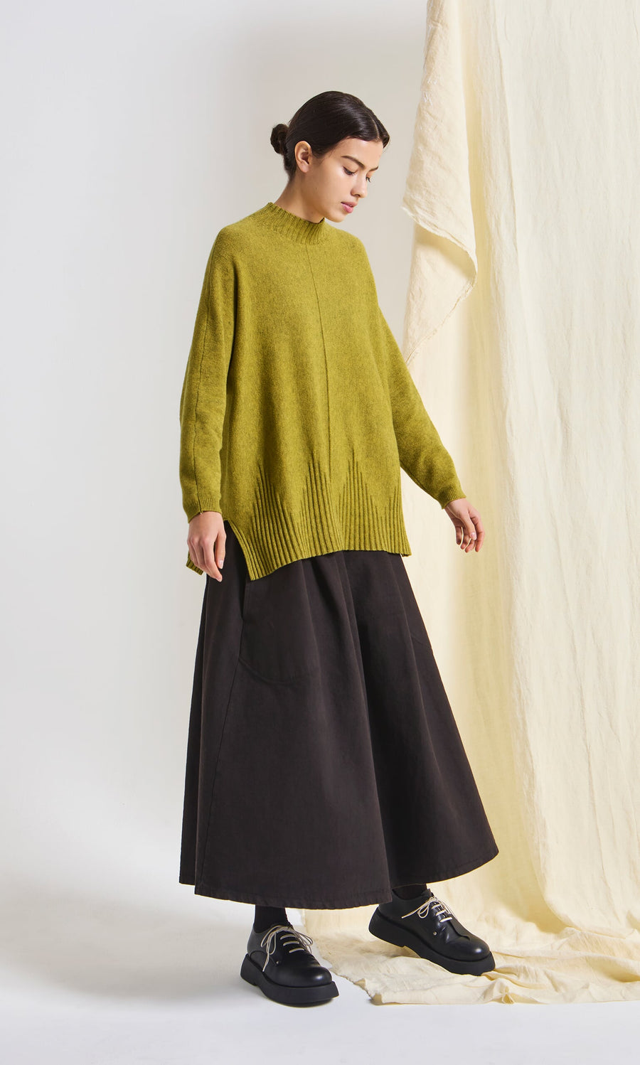 Plümo- Woman wears the Wild Millet Jumper, a loose marled sweater, styled with a wide black skirt against a neutral background.