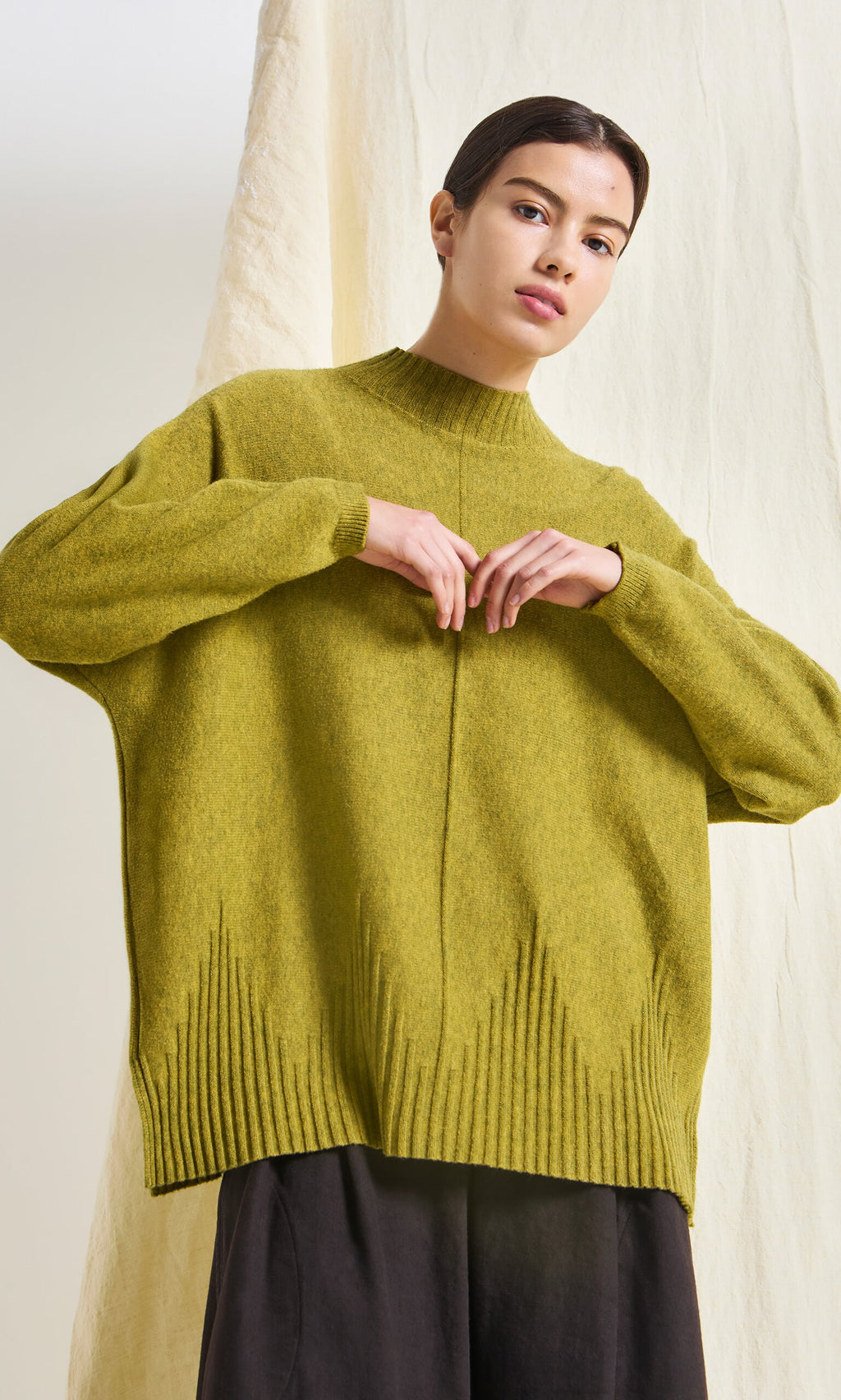 Plümo- Person wearing the Wild Millet Jumper with dark pants, standing against a cream-colored textured backdrop.