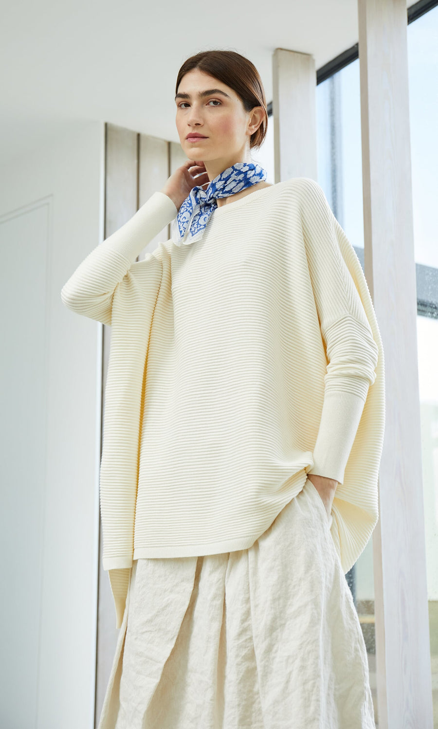 Plümo- Woman wearing the Jack Sweater - Cloud, a cream, super soft ribbed oversized sweater, standing indoors.