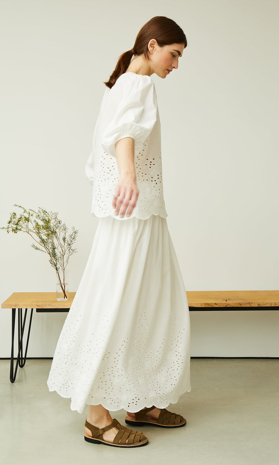 Plümo- A woman in a white blouse and brown sandals walks by greenery wearing the Bright Skirt.