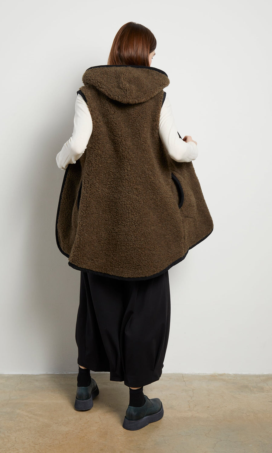 Plümo- Person facing away, wearing the Bigger Rambler Gilet in Peat Brown over a white top, with black baggy pants and dark shoes.
