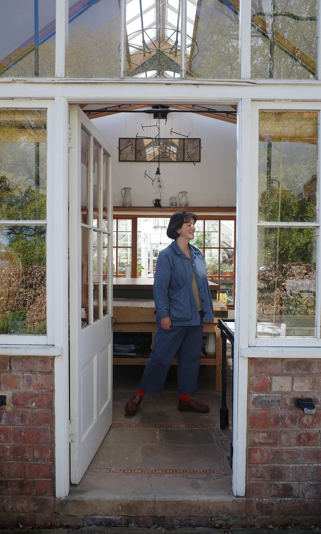 Plümo  A person in blue stands in a greenhouse, inspired by Vegetable Recipes By Jess Dennison, gazing outside.