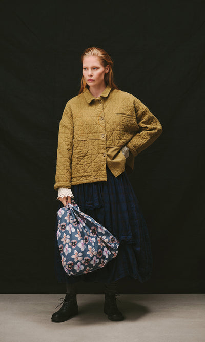 Plümo  A person in a quilted jacket and dark skirt carries a floral Dahlia Tote.