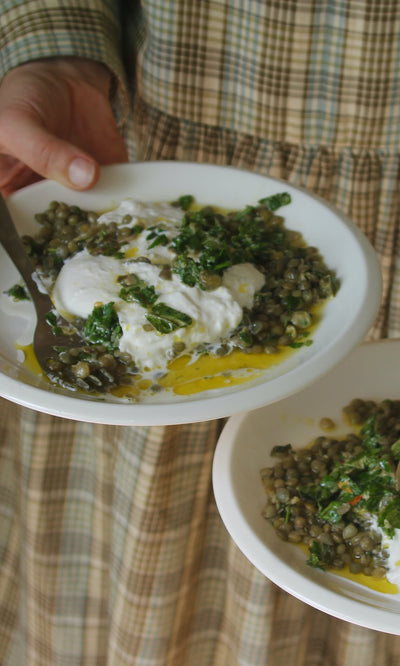 Plümo- A person holds plates of lentils with poached eggs and yogurt from Midweek Recipes By Jess Elliott Dennison.