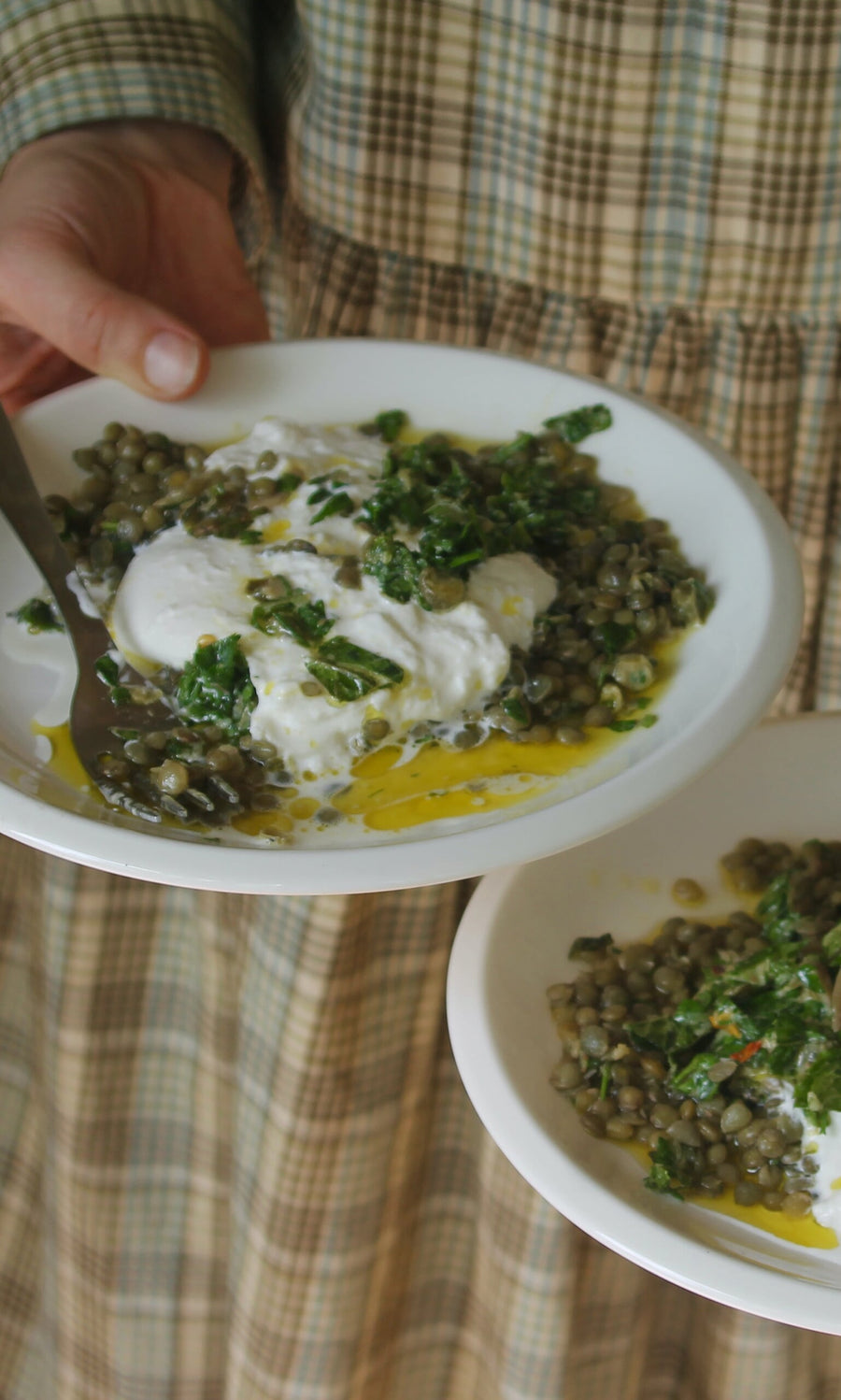Plümo- A person holds plates of lentils with poached eggs and yogurt from Midweek Recipes By Jess Elliott Dennison.