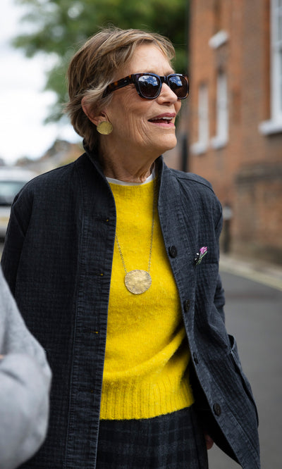 Plümo  The Cressa Necklace features a woman wearing a long sterling silver chain with a large, textured gold brass pebble pendant.