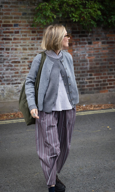 Plümo  A person wears a Grey Melange Cardigan, a striped shirt, and wide-leg trousers while carrying a green shoulder bag.