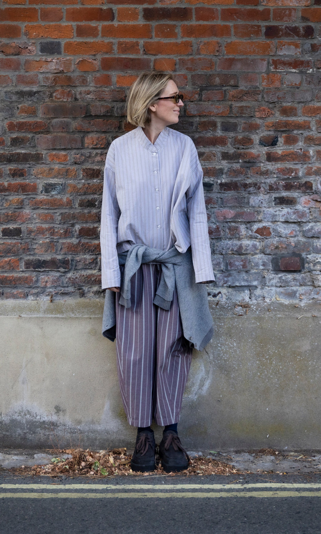 Plümo  A person wears a Bennett Blouse - Smoke with matching trousers and a sweater tied around their waist.