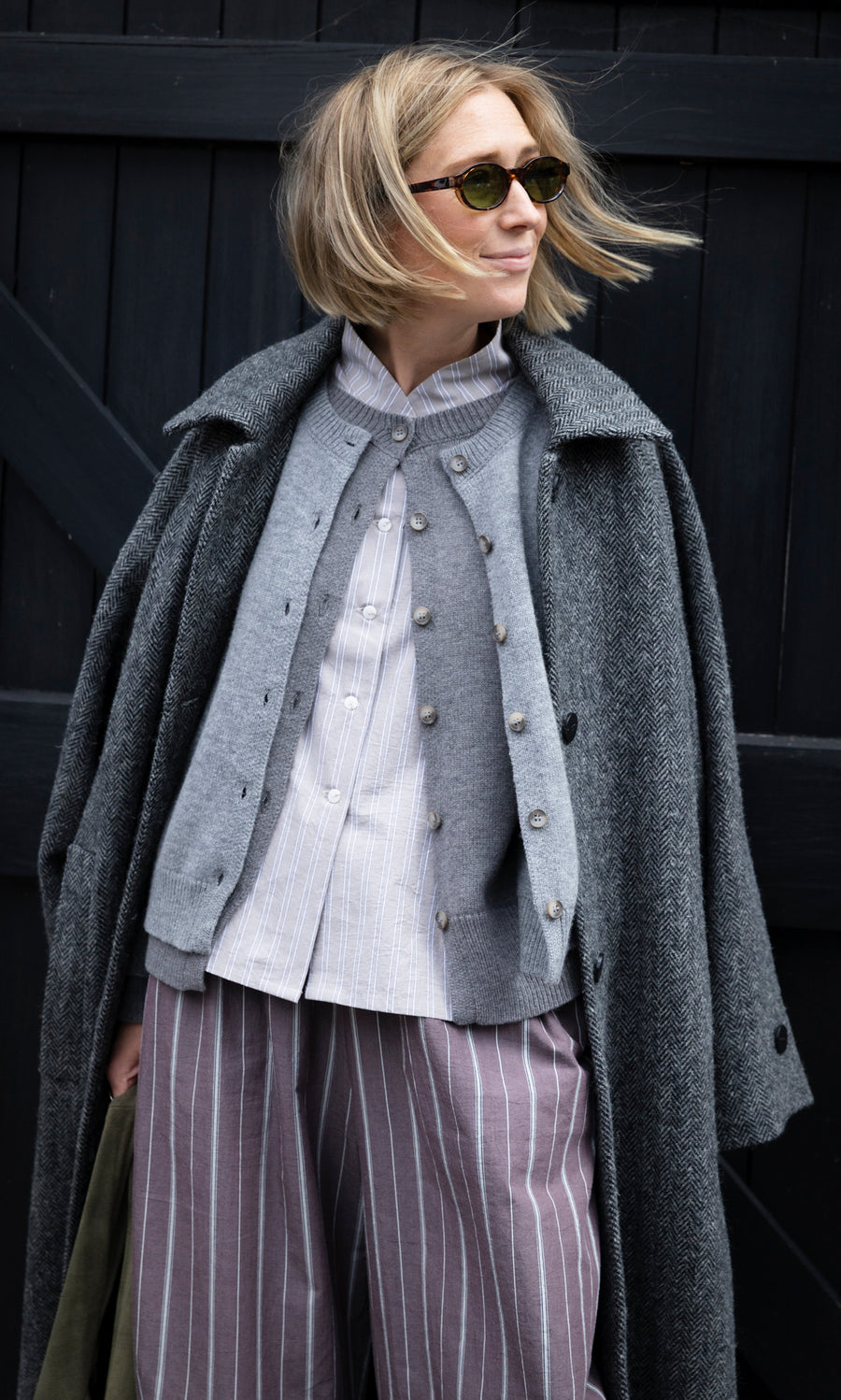Plümo  A woman wearing a Grey Melange Cardigan layered over a striped shirt and a herringbone coat.