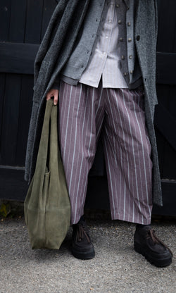 Plümo  A person in a layered coat and striped wide-leg trousers holds an olive green suede Olivia Suede Bag, wearing platform shoes.