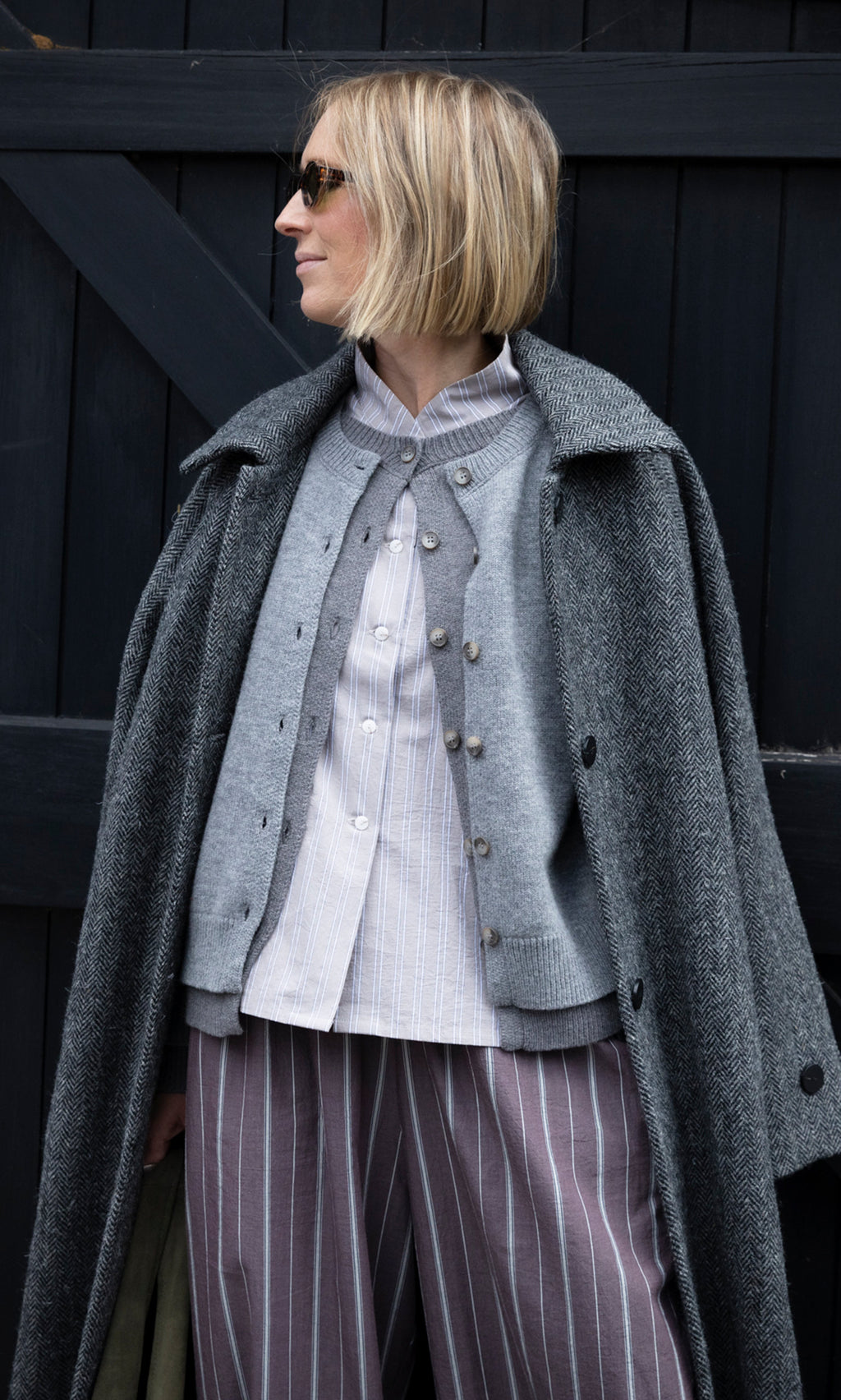 Plümo  A person wears a Bennett Blouse - Smoke with a grey knit cardigan and a herringbone coat draped over them.