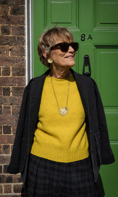 Plümo  A woman wearing Cohen Earrings, which are handmade, textured gold disks, and a matching pendant necklace.