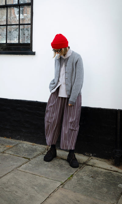 Plümo  A person wearing a Red Breton Beanie, a grey Guernsey jumper, and wide-leg striped trousers.
