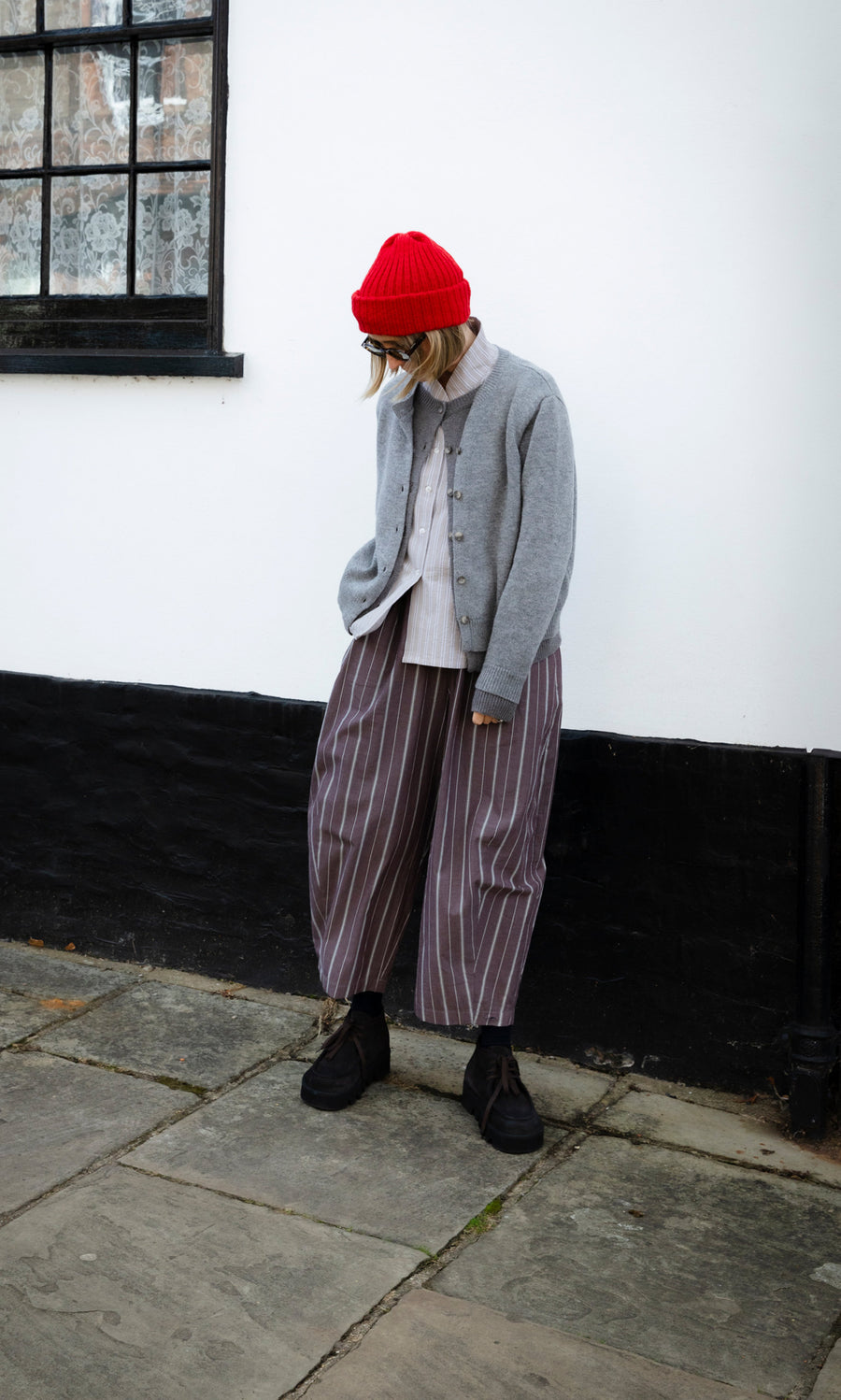 Plümo  A person wearing a Red Breton Beanie, a grey Guernsey jumper, and wide-leg striped trousers.